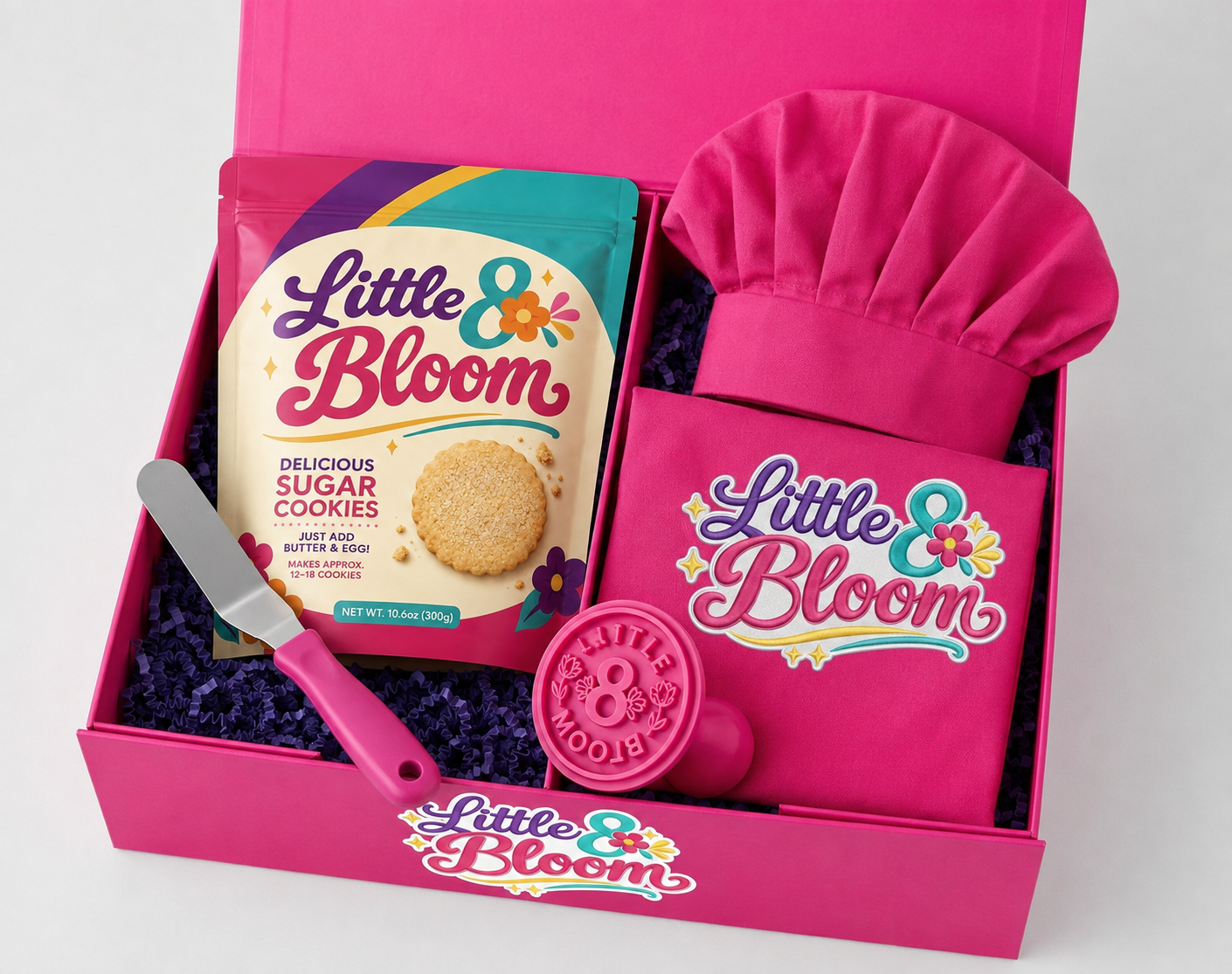 Little 8 Bloom baker welcome kit: hot pink gift box filled with a sugar cookie mix pouch, pink chef hat, logo apron, offset icing spatula and Little 8 Bloom cookie stamp
